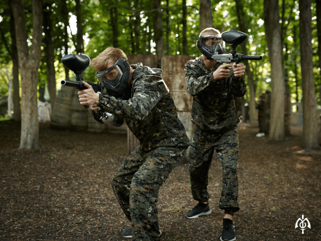 Adrenalinski pokloni: 7 ideja za poklon koji se pamti 2 dva prijatelja stoje na poziciji dok igraju paintball, adrenalinski pokloni